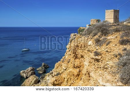 Malta - Sail boat at Ghajn Tuffieha tower on a hot summer day with crystal clear blue sea water