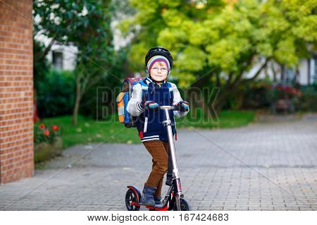 Active school kid boy in safety helmet riding with his scooter in the city. Happy child in colorful clothes biking on way to school. Safe way for kids outdoors to school.
