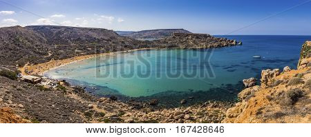 Malta - Panoramic view of Ghajn Tuffieha sandy beach with sail boat blue sky and crystal clear green sea water