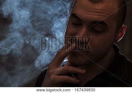 Young desperate caucasian man with cigarette in hands. Smoky background. Bad habits concept.