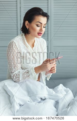 Woman in the bed reading a message on your phone.