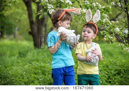 Two Little Kids Boys And Friends In Easter Bunny Ears During Traditional Egg Hunt In Spring Garden,