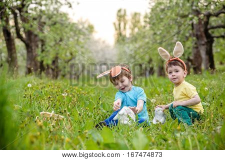 Two Little Kids Boys And Friends In Easter Bunny Ears During Traditional Egg Hunt In Spring Garden,