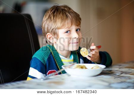 Adorable little school boy eating pasta indoor. Blond child in domestic kitchen or in school canteen Cute kid and healthy food, ravioli or russian pelmeni.