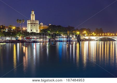 Dodecagonal military watchtower Golden Tower or Torre del Oro and Guadalquivir river during evening blue hour, Seville, Andalusia, Spain