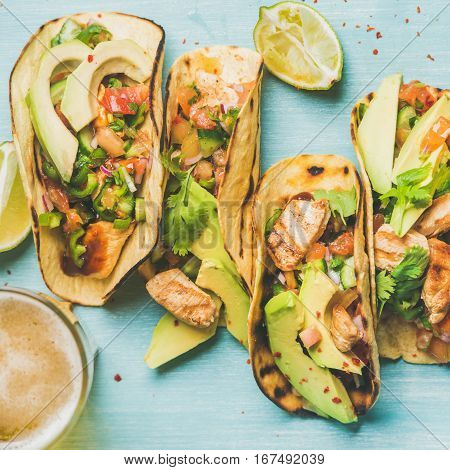 Healthy corn tortillas with grilled chicken, avocado, fresh salsa, limes and beer in glass over blue wooden background, top view, square crop. Gluten-free, allergy-friendly, weight loss concept