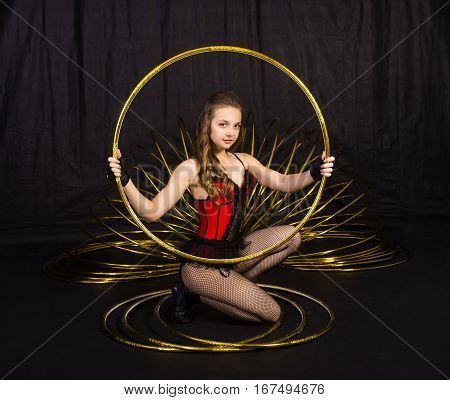 A gymnast sitting with hula hoop on dlack background. Studio photography of circus performers.