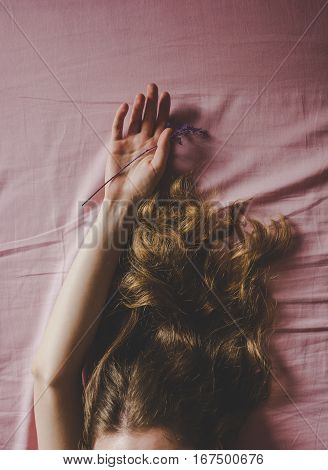 young woman lying on the bed with a pink bedsheet, soft daylight from the side, beautiful line of hand with branch plants, curly hairs.