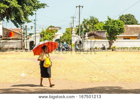 Yogyakarta, Indonesia - September 2, 2015: Old woman walking over square in the sun with umbrella next to Kraton