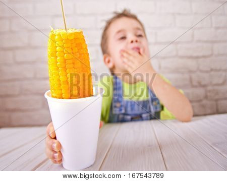 Cute boy holdind boiled sweet corn in cup on white bricks wall background.