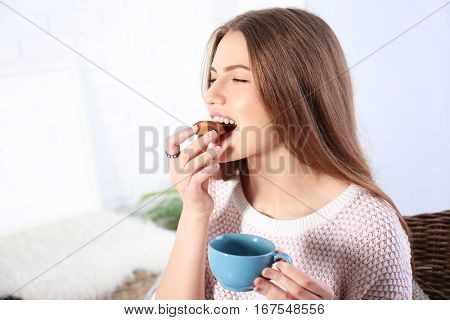 Young woman eating cookie with coffee in living room