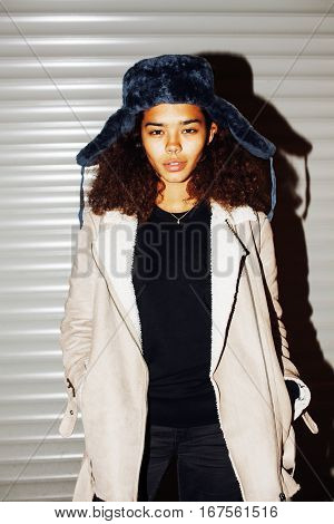 young pretty african american girl teenage outside on street, looking like real junky, social issues concept, red eyes, bum stupid hat, fashion hipster lifestyle people close up mudy
