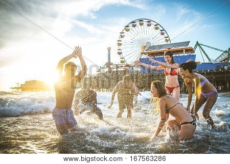 Group of friends splashing water while swimming in the sea - Multi-ethic group of people having fun on the beach