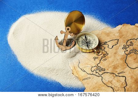 Compass, anchor and old map in sand on blue background. Columbus Day concept