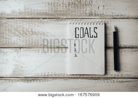 Goals concept. Notebook with goals list on wooden table. Motivation strategy write idea success solution concept. Top view. Retro toned image. Copy space