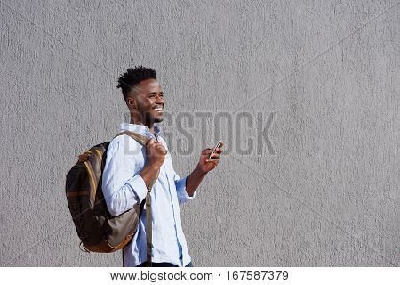Handsome Black Man With Bag And Cellphone Walking By Wall