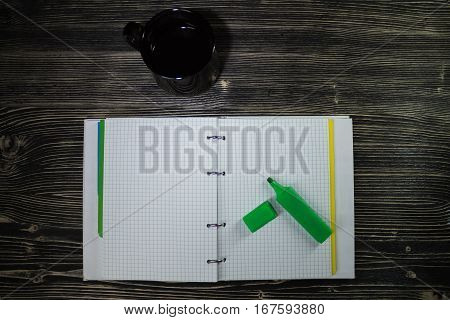 Top view of open notebook on which there is a green marker and next is a Cup of coffee.