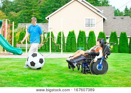 Caucasian father playing soccer with ten year old biracial disabled son in wheelchair at park outdoors