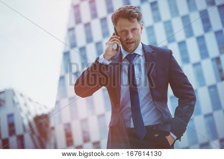 Low angle view of confident businessman speaking on mobile phone against office building