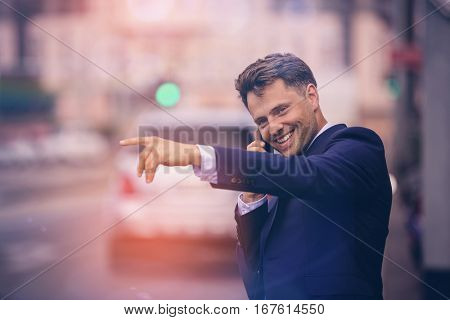 Handsome businessman hailing taxi while taking on phone at street