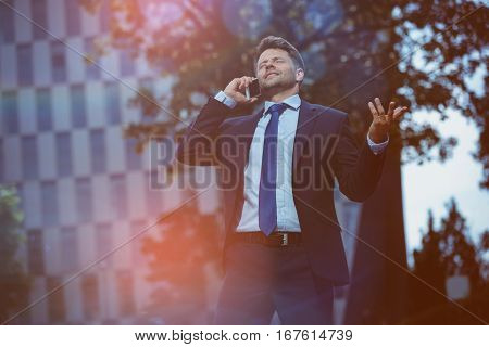 Handsome businessman discussing on mobile phone near office building