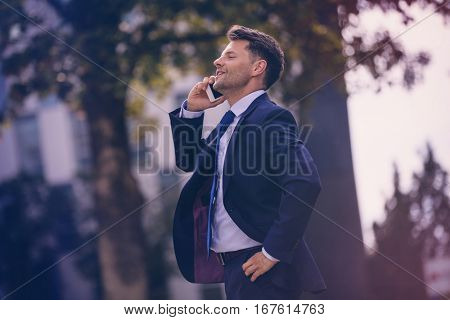 Confident businessman talking on mobile phone against tree