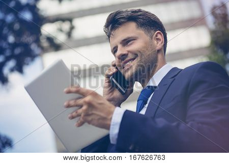 Low angle view of cheerful businessman with mobile and digital tablet outside office