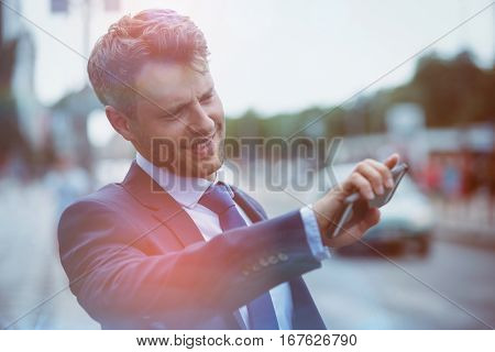 Handsome businessman holding mobile phone and hailing taxi at street