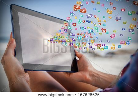 Woman sitting on beach in deck chair using tablet pc against colourful computer applications 3d