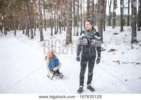 Young couple walking and sledding in the winter in the forest during a snowfall