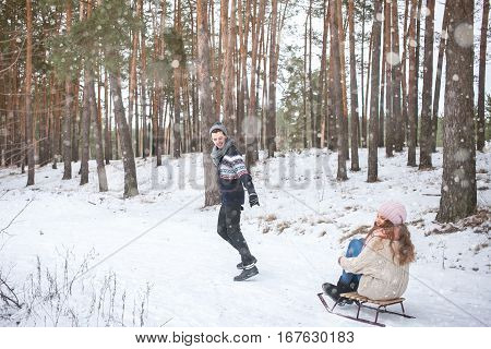 Young couple walking and sledding in the winter in the forest during a snowfall