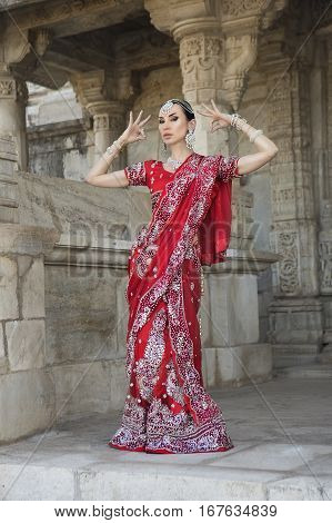 Beautiful Maharani Namaste. Young Indian Woman in Red bridal Sari clothing with bridal oriental jewelry. Beautiful Bollywood Girl in wedding Sari. Indian Bride in Ranakpur Jain Temple Rajasthan