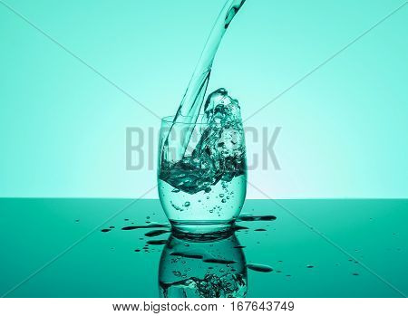 Bottle with creative splashing water in the glass on turquoise background.