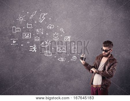 An elegant hipster guy trying to use a vintage camera with camera settings icons drawn on wall, like flash, white balace or ISO value concept