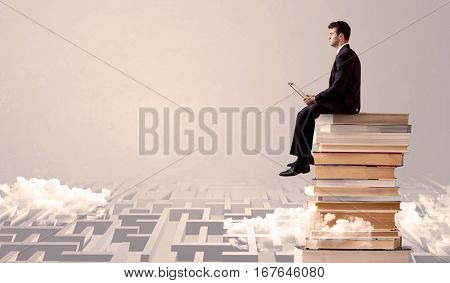 A businessman with laptop tablet in elegant suit sitting on a stack of books on top of sandy labirynth background concept