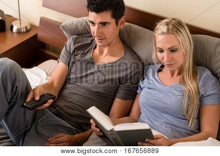 Young couple sitting in bed while relaxing with different hobbies