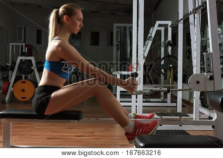Attractive young fitness model in black-blue sportswear works out on training apparatus in fitness center