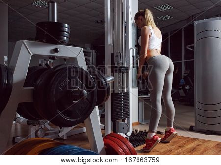 Sexy blond girl with a perfect figure and a great ass in gray leggings trains in fitness club