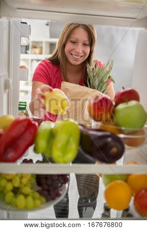 Young housewife put peppers from market in fridge