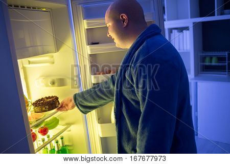 At night corpulent  guy take chocolate cake from refrigerator dangerous for obese