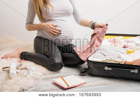 Woman packing baby clothes for hospital and taking notes