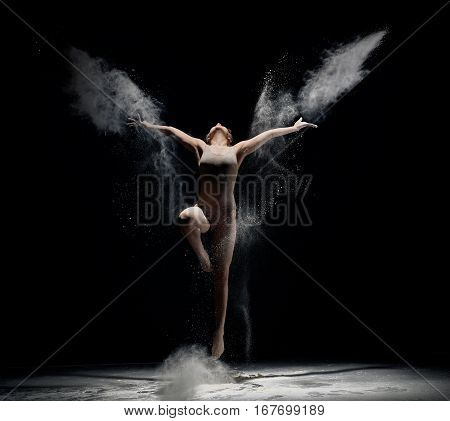 Slender girl dancing in white powder cloud jumping and streching up studio shot