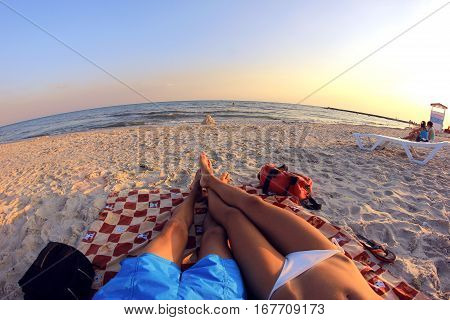 Couple man and woman sunbathing on the beach overlooking the sea. They lie on a mat on the sand. In front of them a house of sand and water. Around other people are resting. Ukraine, Black Sea coast