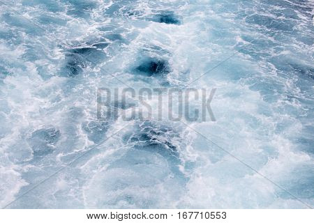 Blue water background. Foamy wave on sea water made by cruise ship. Pacific ocean surf after motor boat. Splashes and drips of oceanic water. White water ornament on marine surface. Cruiseliner tail