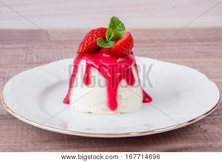 panna cotta dessert with strawberry sirup and mint leaf on light wooden background