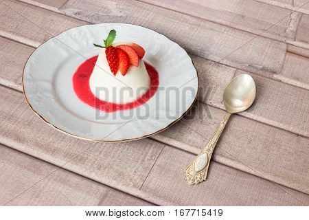 panna cotta dessert with strawberry sirup and mint leaf with spoon on light wooden background