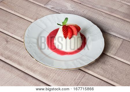 panna cotta dessert with strawberry sirup and mint leaf on light wooden background