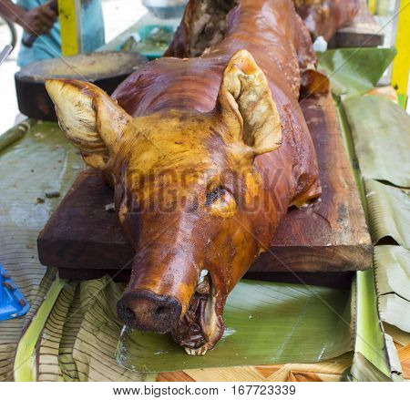 Whole roasted pig on eatery table. Meat market in Philippines. Roasted pork ready for serving. Grilled piglet with head. Whole pig baked with crispy skin. Delicious pork meat for lunch. Cooked jamon