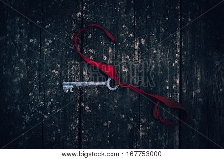 an antique rusty key on red ribbon on vintage wooden board