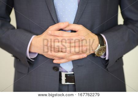 Hands of man in suit poses with folded hands and wristwatch in studio, noface